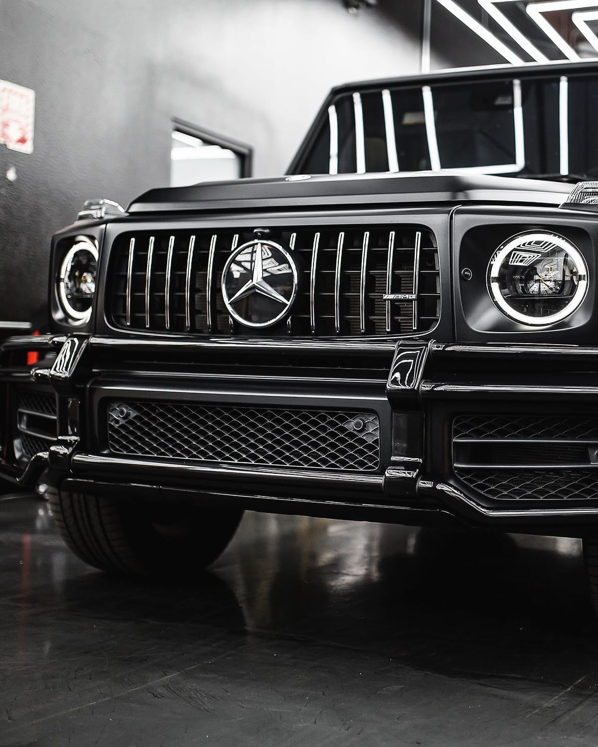 A matte black Mercedes-AMG G 63 under a grid of ceiling lights.