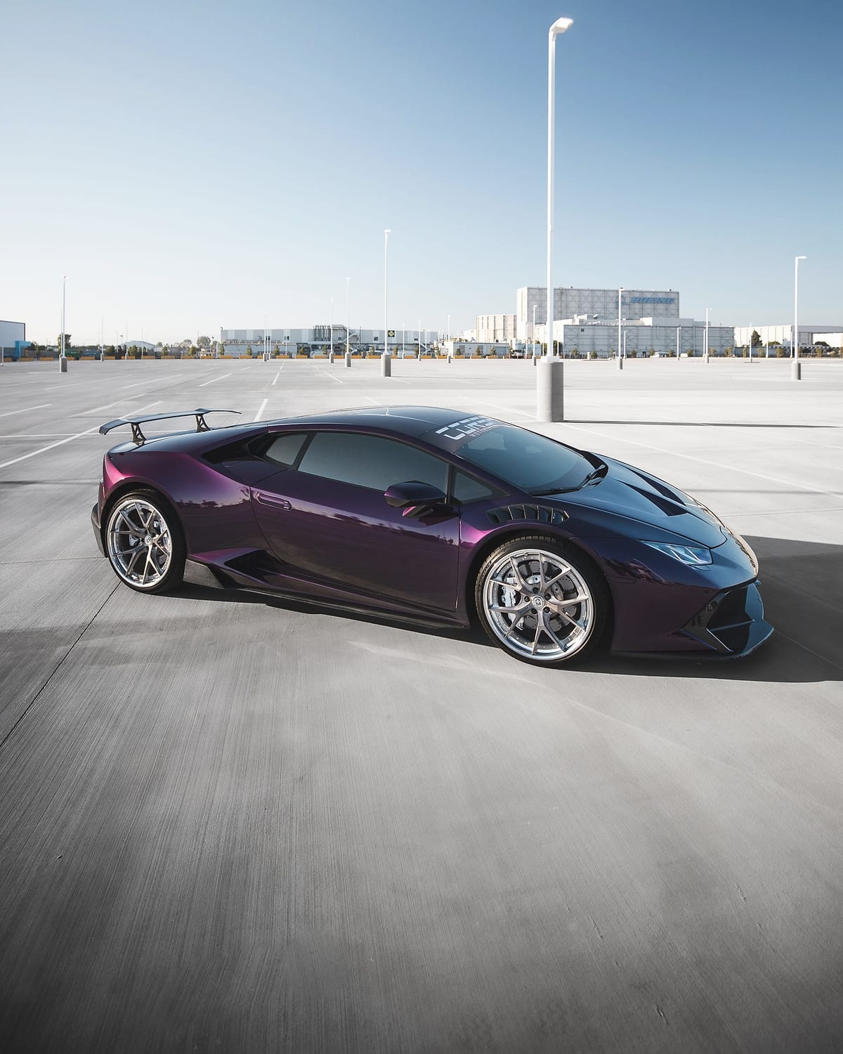 A purple Lamborghini Huracán with a tall rear wing on pale concrete.