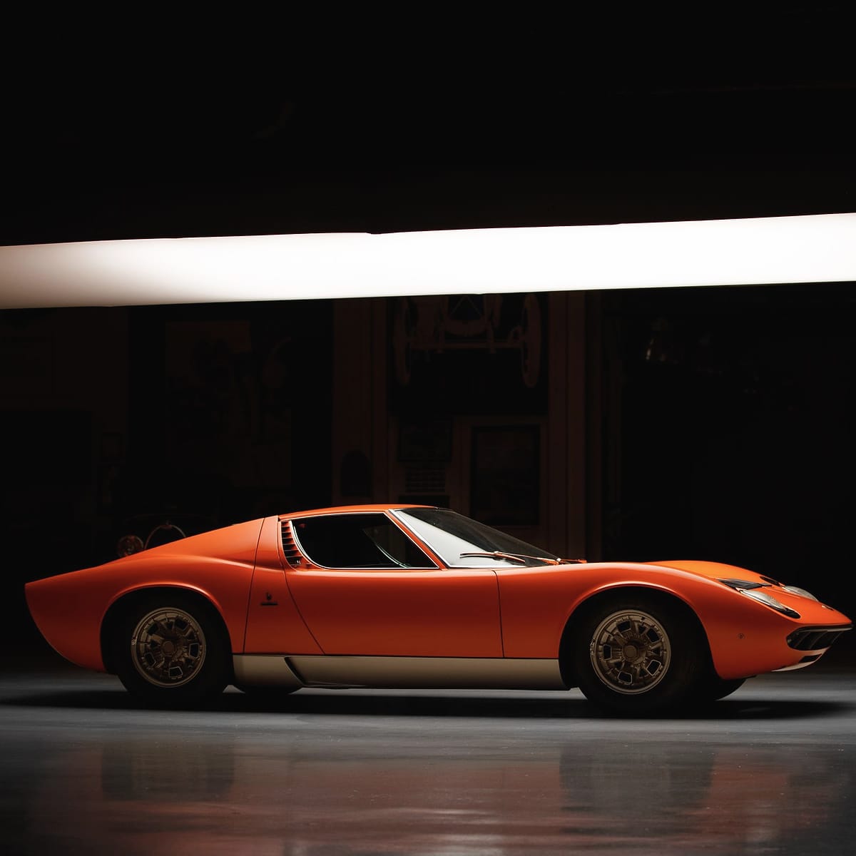 An orange Lamborghini Miura in profile under one long soft light.