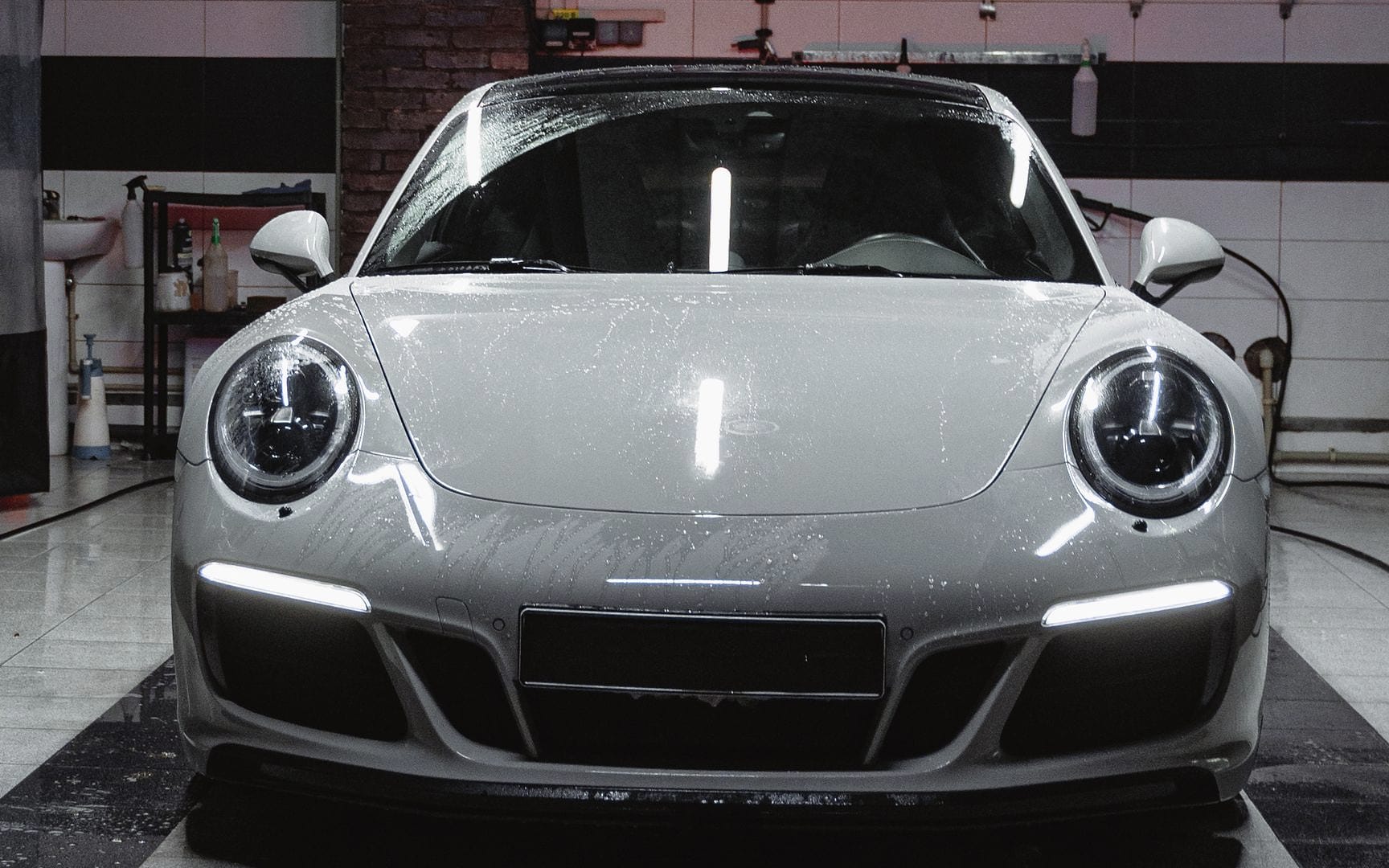 A silver-grey Porsche 911 faces the camera in a dark, wet bay.
